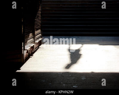 Stadt Einsamkeit: Schatten einer Person allein wandern und geschlossener u Shop am Sonntag Morgen in sepia schwarz und weiß Stockfoto