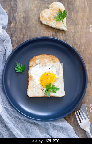 Ei in einen herzförmigen Brot mit Petersilie, romantisches Frühstück. Selektive konzentrieren. Stockfoto