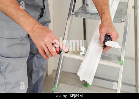 Installation von Stuckdecken. Arbeitnehmer setzt Leim auf Spritzgussmaschinen für die Befestigung an der Decke Stockfoto