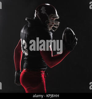 US-amerikanischer Footballspieler posiert mit Ball auf schwarzem Hintergrund Stockfoto