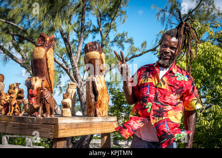 Ein lächelndes Holzschnitzer Handwerker mit geschnitzten Tiere auf Anzeige, Verkauf von Holz- Eulen, Elefant Schnitzereien an Touristen in der Nähe von Fincastle in Nassau, Bahamas Stockfoto