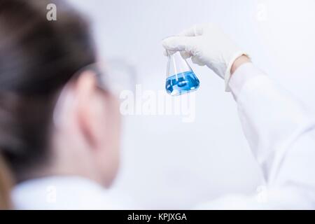 Laboratory Assistant Holding chemische Flasche mit blauer Flüssigkeit. Stockfoto