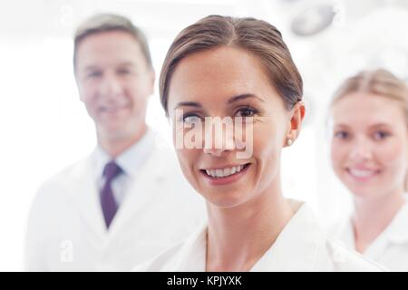 Ärztin in Richtung Kamera lächelnd, zwei Ärzte im Hintergrund. Stockfoto