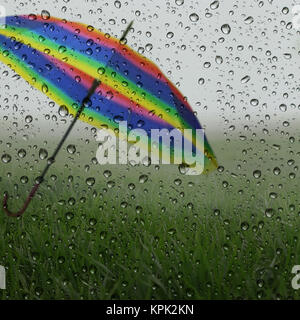 Nasses Glas mit Regentropfen, grünes Gras und bunten Regenschirm Stockfoto