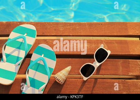 Flip Flops und Sonnenbrille auf Holzbohlen und Wasser Stockfoto