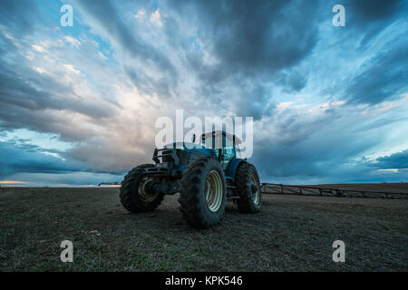 Traktor in einem Feld unter einem dramatischen Himmel bei Sonnenuntergang geparkt; Val Marie, Saskatchewan, Kanada Stockfoto