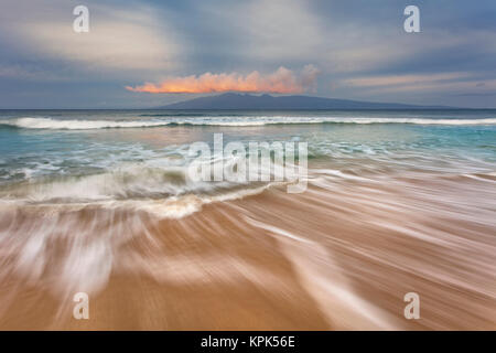 Weiches Wasser erstreckt sich über den Sand bei Sonnenaufgang mit Blick auf Molokai; Maui, Hawaii, Vereinigte Staaten von Amerika Stockfoto