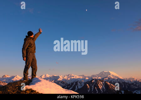 Ein Mann auf den Mond zeigt, die über Denali von der Spitze eines schneebedeckten Grat bei Sonnenuntergang in der Nähe von Polychrome Berg in Denali National Park Stockfoto