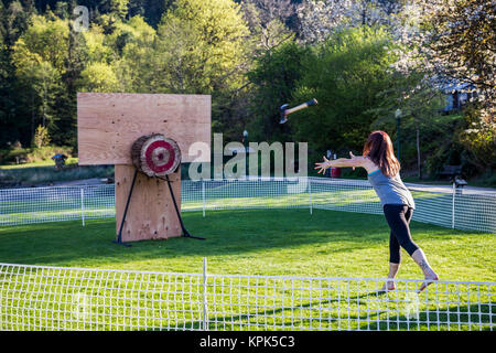 Eine Frau wirft eine Axt an ein Ziel in einer entspannenden Axtwerfen Spiel während einer Protokollierung Festival; Bowen Island, British Columbia, Kanada Stockfoto