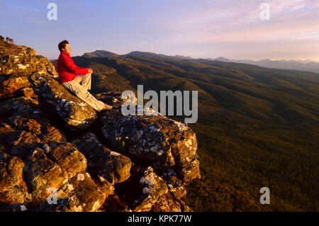 Abenteuerliche Frau sitzt auf einer hohen Klippe Fels an der Oberseite der Reed Lookout in den Grampians National Park (Gariwerd), Victoria, Australien Stockfoto