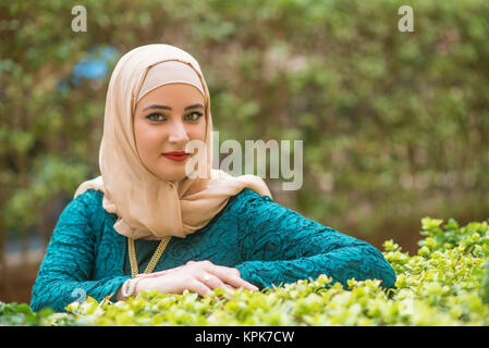 Schöne junge muslimische Frau mit Kopftuch stützte sich auf die Pflanzen im Freien Stockfoto