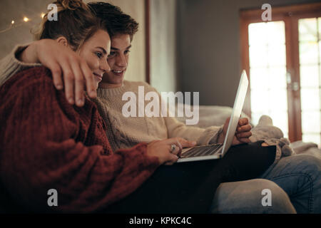 Mann und Frau sitzt auf der Couch und schaut auf einen Laptop. Paar mit Laptop im Wohnzimmer. Stockfoto