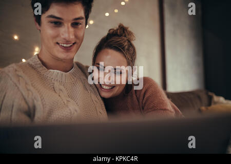 Lächelnden jungen Mann und Frau mit Laptop zu Hause. Hygge Paar sitzt auf einem Sofa mit einem Laptop im gemütlichen Wohnzimmer. Stockfoto