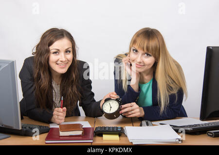 Zwei Mädchen im Büro mit der Uhr erwarten glücklich am Ende des Arbeitstages Stockfoto