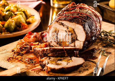 Lecker Schweinebraten in Scheiben schneiden und u 200 bu 200 bwith Füllung auf Schneidebrett neben Schüssel gekochten Rosenkohl und Gabel Stockfoto