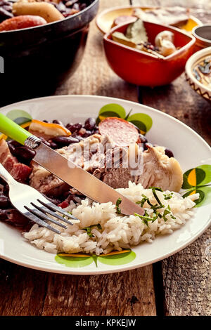 Traditionelle würzige brasilianische Feijoada Eintopf mit Schweinerippchen, Chorizo Wurst und schwarze Bohnen auf einem Teller serviert mit herzhaften Reis für ein nationales Gericht Stockfoto
