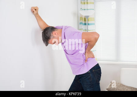 Mann, der Rückenschmerzen während lehnte sich auf weiße Wand Stockfoto