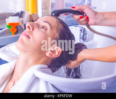 Frau mit dunklen langen Haaren in Haar in ein Waschbecken der Friseursalon durch einen Friseur mit roten Nägeln gewaschen. Stylist hält Kunden Haar, während es Benetzung Stockfoto