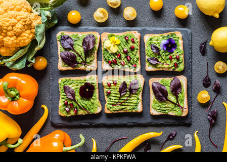 Frühstück verschiedenen avocado Sandwich. Verschiedene frische bunte Bio Gemüse. Gesunde Rohstoffe veganes Essen auf grauem Hintergrund. Stockfoto