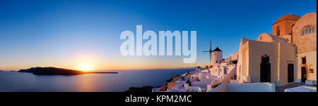 Sonnenuntergang über der Insel Santorini in Griechenland. Traditionelle Kirche, Apartments und Windmühlen im Dorf Oia auf einen Sonnenuntergang, panorama bild. Stockfoto