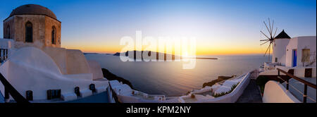 Sonnenuntergang über der Insel Santorini in Griechenland. Traditionelle Kirche, Apartments und Windmühlen im Dorf Oia auf einen Sonnenuntergang, panorama bild. Stockfoto