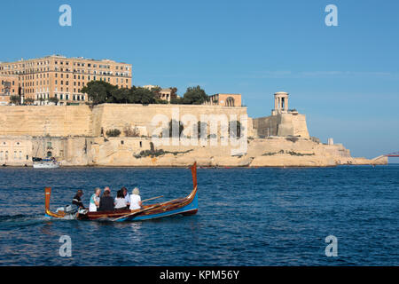 Touristen auf einem traditionellen maltesischen dghajsa Fähre in Malta Grand Harbour mit den Befestigungsanlagen von Valletta im Hintergrund. Reise und Tourismus. Stockfoto