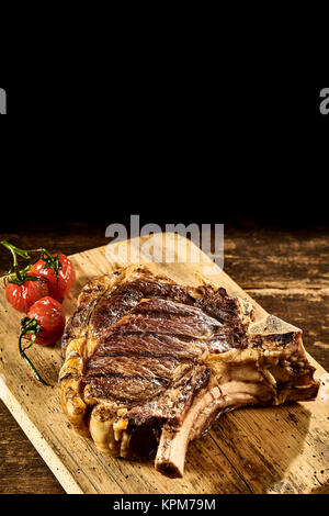 Drei gebratene Tomaten und Servieren von Cote de boeuf Steak mit Fett und Grill Markierungen auf Schneidebrett über Holz- Hintergrund Stockfoto