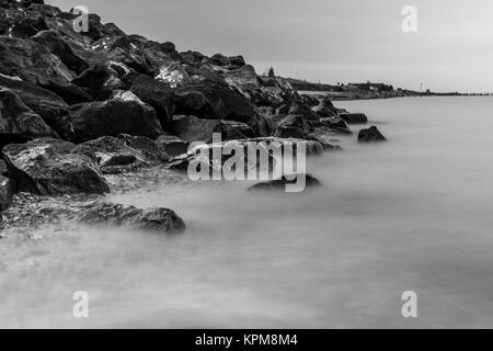 Wellen über die Felsen am Strand in Essex Stockfoto