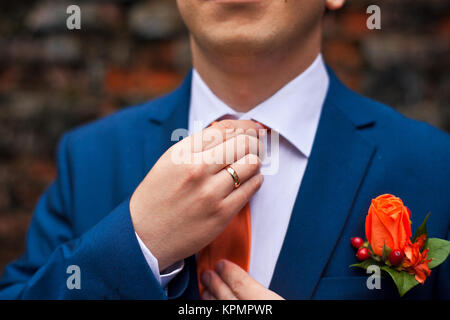 Der Bräutigam in einem blauen Anzug passt seine orange tie Stockfoto