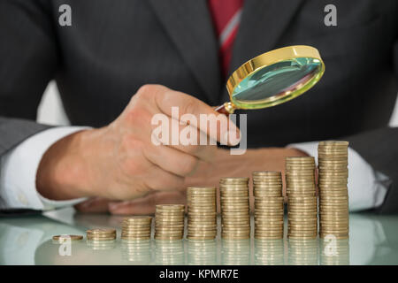 Geschäftsmann Holding Lupe auf Münze am Schreibtisch Stockfoto