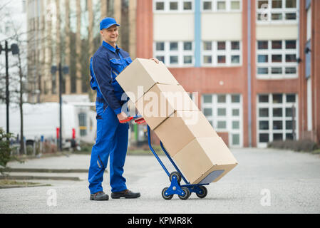 Deliveryman Holding Trolley geladen mit Kartons Stockfoto