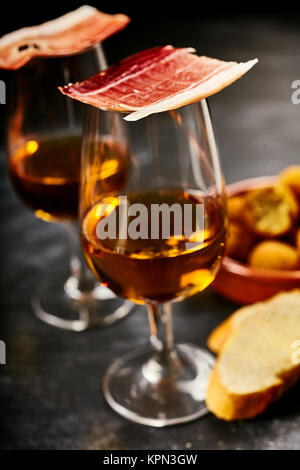 Traditionelle spanische Tapas serviert mit Sherry Aperitif in eleganten Brille mit Gourmet Schinken Balancing auf der Oberseite neben geschnittenem Baguette und bacalao Kroketten Stockfoto