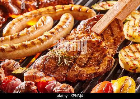 Köstliches Angebot an Fleisch Hals Steak und Gemüse grillen auf ein BBQ mit Würstchen, Koteletts, Spieße mit gemischten Kebabs, Paprika und Auberginen in der Nähe zu sehen, mit der Zange drehen ein Schnitzel Stockfoto