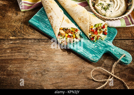 Hohen Winkel noch Leben auf Paar Chicken Fajitas gefüllt mit frischem Gemüse auf abgenutzten Blau Holz Schneidebrett auf rustikalen Holztisch mit Dip Sauce und Stoffservietten und reichlich Platz kopieren Stockfoto