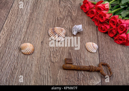 Rostiger Schlüssel, sea shell und Rosen auf einem hölzernen Hintergrund Stockfoto