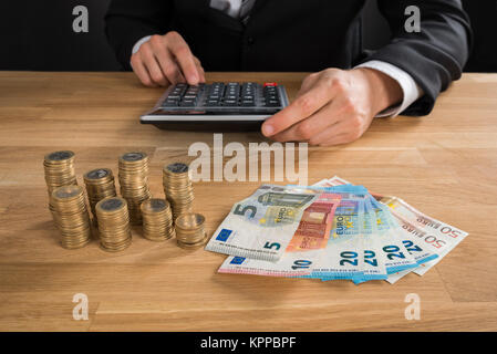 Geschäftsmann mit Taschenrechner mit Münzen und Banknoten Stockfoto