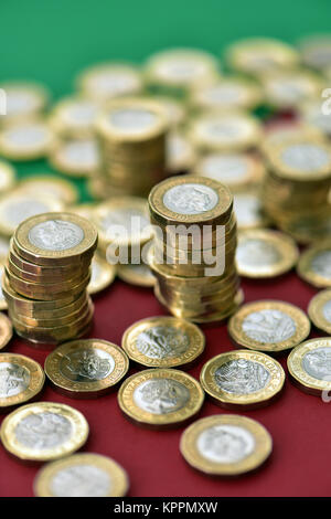 Eine große Anzahl von einem Pfund Münzen auf einer Fläche und in Stapeln auf eine Rote und Grüne Weihnachten farben Hintergrund verstreut. Weihnachten Ausgaben und Schulden. Stockfoto