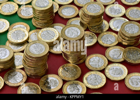 Eine große Anzahl oder Sammlung von einem Pfund, die Münzen auf eine Rote und Grüne Weihnachten farbigen Hintergrund mit Stapel von Münzen in einer Zählung Haus verstreut. Stockfoto