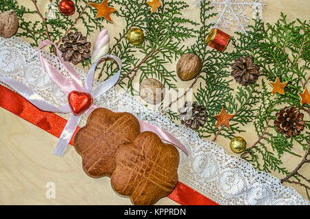 Zwei cookies mit roter Spitze und Band, Schokolade Herz am Bogen und Zweige von thuja, stehen in einem Winkel auf Holz Sperrholz Stockfoto