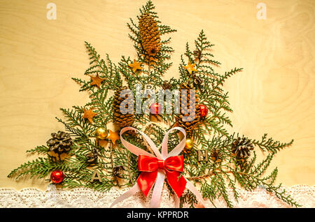 Helles Holz Sperrholz mit einem Weihnachtsbaum, aus Zweigen Thuja mit Tannenzapfen und Schokolade Kugeln auf einem lace Ribbon Stockfoto