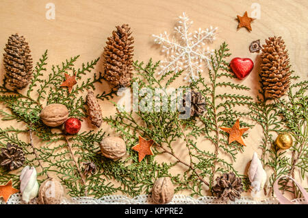 Weihnachten Hintergrund aus Holz Sperrholz mit Schokolade Herzen und Kugeln, Tannenzapfen, Nüsse mit Schneeflocke liegen auf den Ästen eines Thuja Stockfoto