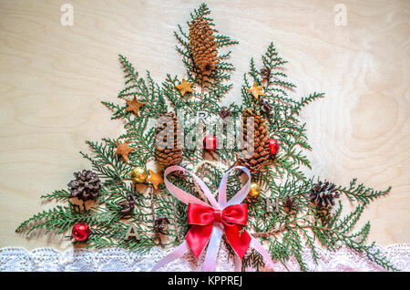 Licht Sperrholz mit einem Weihnachtsbaum, aus Zweigen Thuja mit Tannenzapfen und Schokolade Kugeln auf einem lace Ribbon Stockfoto