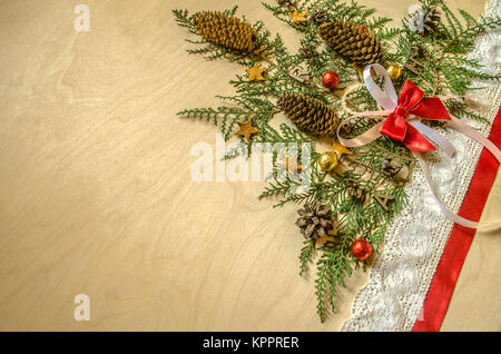 Weihnachtsbaum wird aus Zweigen von thuja mit Tannenzapfen und Schokolade Kugeln, Rot und Spitze Band in einem Winkel auf Sperrholz gesammelt Stockfoto