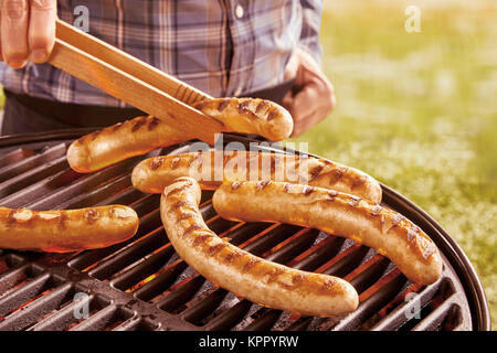 Nicht identifizierbare Person mit hölzernen Zange verschiedene Hot Dog Würstchen auf heißen Grill im Freien sich zu drehen Stockfoto