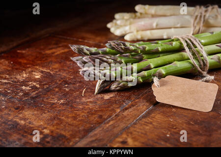 Selektiver Fokus Nahaufnahme von weißem und grünem Spargel Tipps bei Stammzellen mit braunen String und leer Verkauf Tag mit copy Raum über abgenutzten Holztisch gewickelt Stockfoto