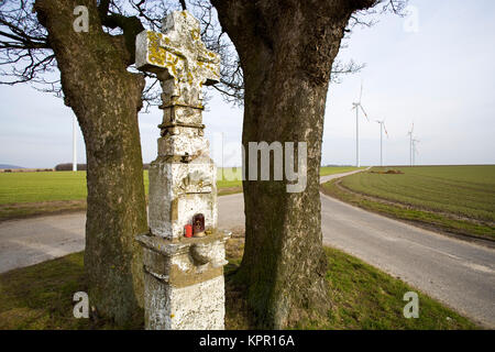 Europa, Deutschland, Kreuz am Straßenrand in der Nähe von Bedburg, im Hintergrund der Windenergieanlagen. Europa, Deutschland, Wegkreuz bei Bedburg, im Hintergrung Windkra Stockfoto