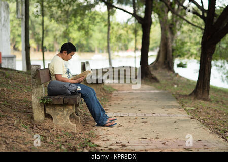 Jungen asiatischen Jungen Lesen eines Buches auf der Bank im Park. Bildung Konzept Stockfoto