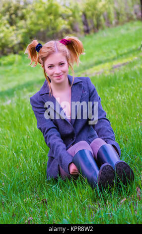 Fröhlicher junger Mädchen sitzen auf dem grünen Rasen Stockfoto