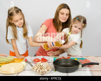 Zwei kleine Mädchen am Küchentisch mit Begeisterung zu helfen, meine Mutter, Pflanzenöl in einer Pfanne gießen Stockfoto