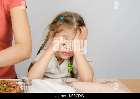 Kleines Mädchen am Küchentisch müde seine Augen reiben, während Mama kocht Stockfoto